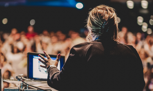 Une femme fait une présentation devant une salle comble.