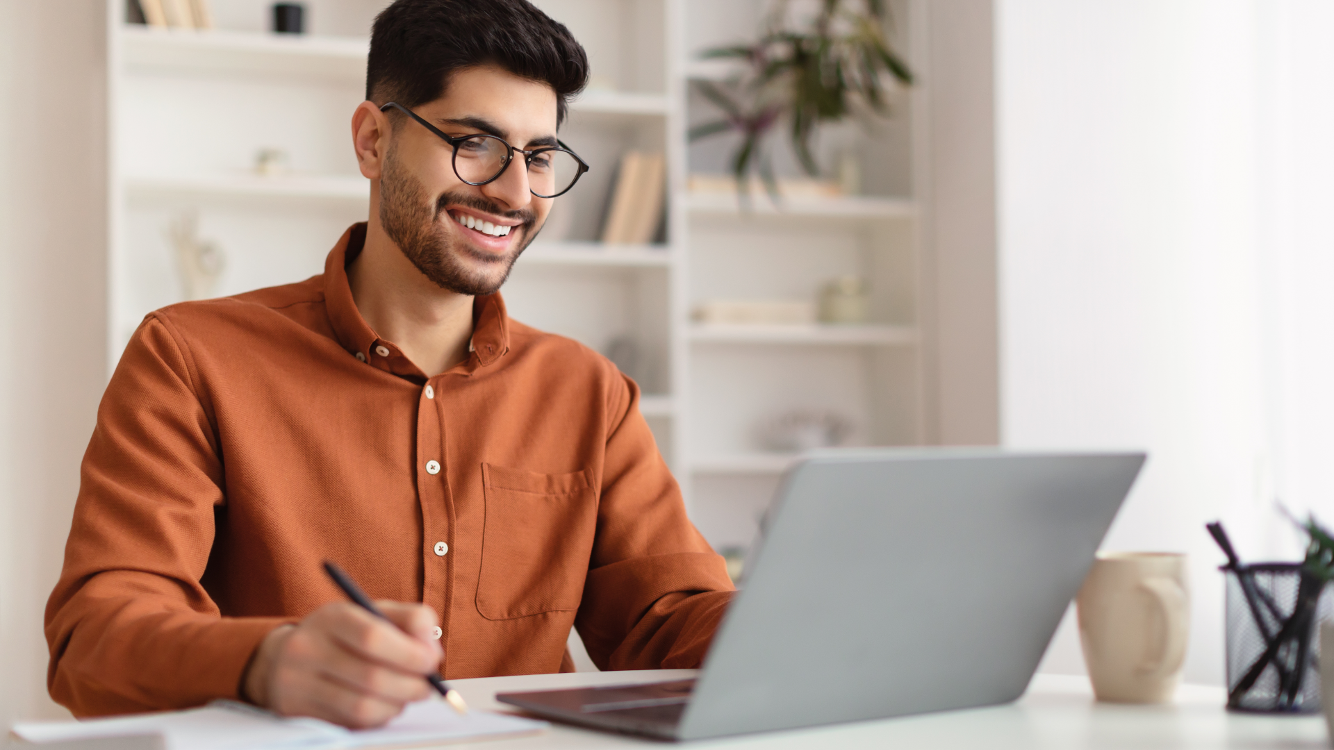 Man looking at laptop with pen in hand.