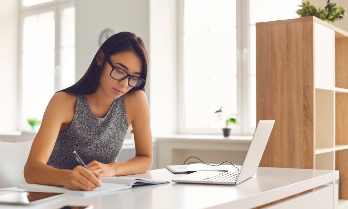 Female writing next to laptop 