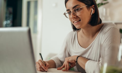 Mujer frente al portátil tomando notas.