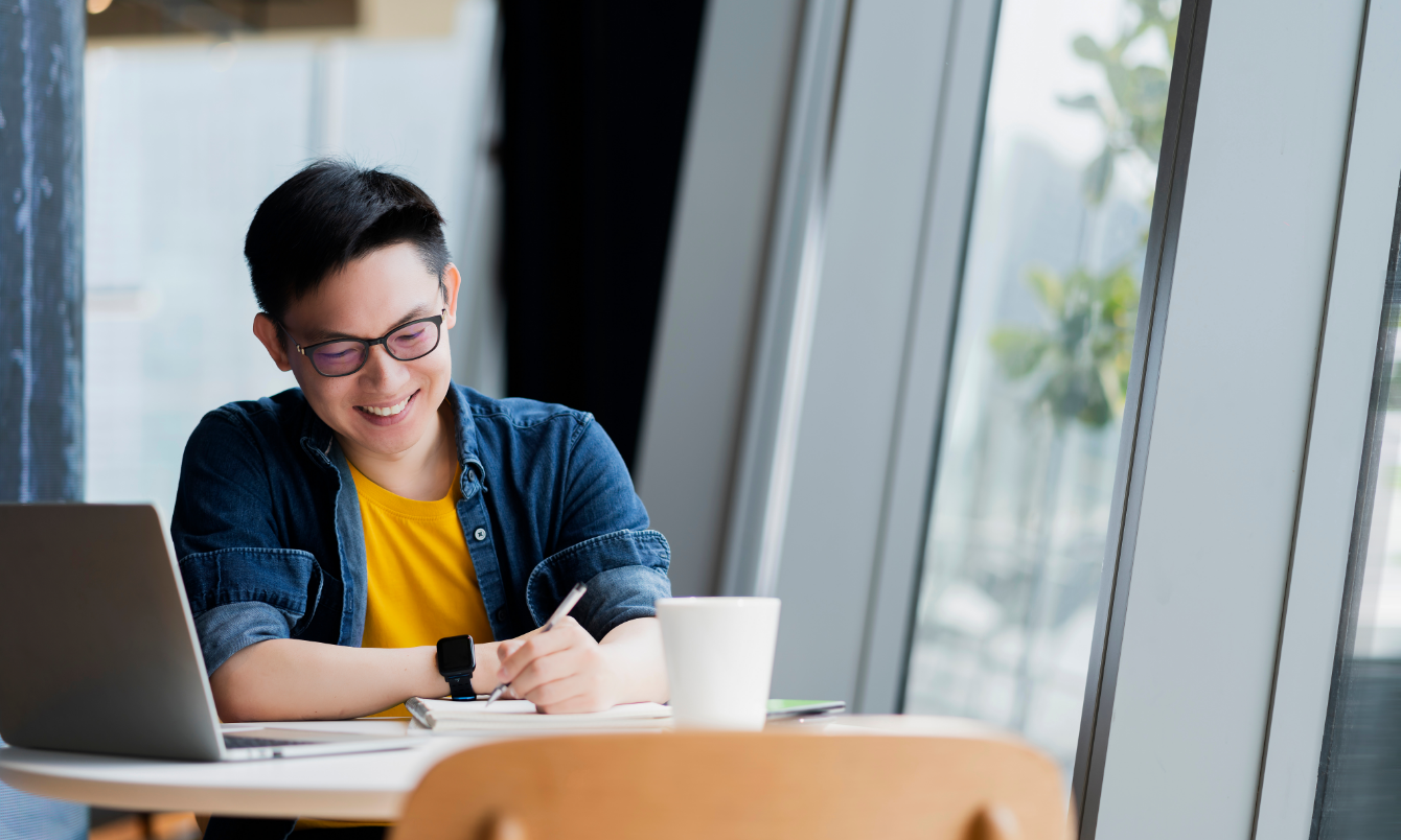 Male writing next to laptop