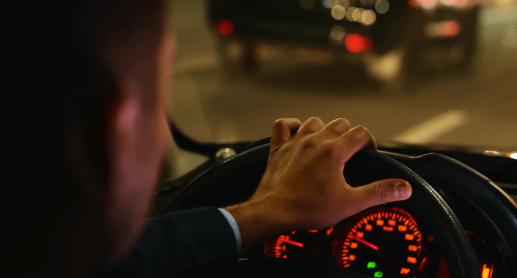 Man behind wheel of car at night time.
