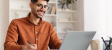 Man looking at laptop with pen in hand.