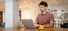 Man typing on a laptop. A yellow espresso cup and saucer sits on a table to his left.