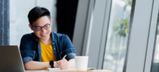 Male writing next to laptop