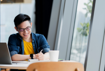 Male writing next to laptop